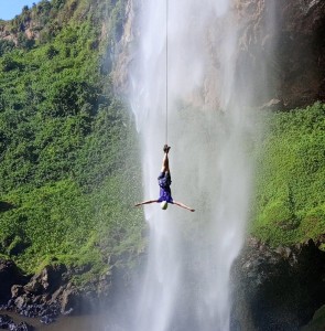A climber abseiling down the cliff beside the falling water at Sipi Falls.