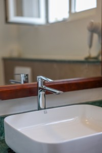 A basin and mirror in a guest bathroom, tiled in green marble.