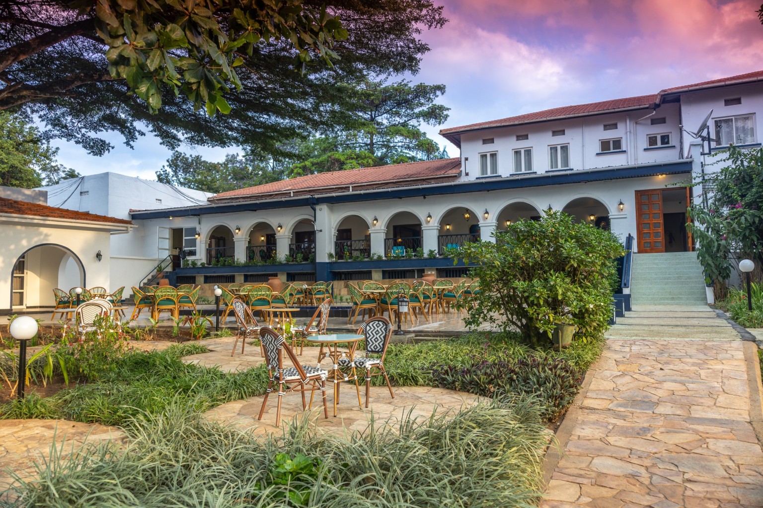 Garden furniture on the lawn under mature trees with the arcaded hotel wing beyond.
