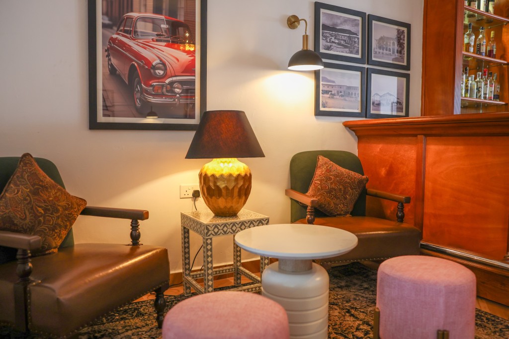 Two leather armchairs and a low round table in the 1950s Bar, a lamp lit between them under framed prints.