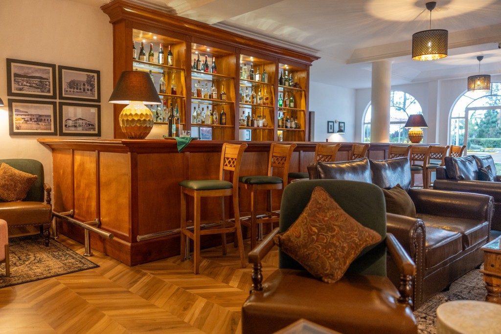 The 1950s Bar: a polished timber counter and stools backed by lit shelves of spirits, with leather armchairs in front.
