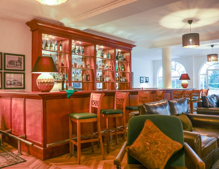 The shelved spirits and timber counter of the 1950s Bar, with stools and leather armchairs in front of it.