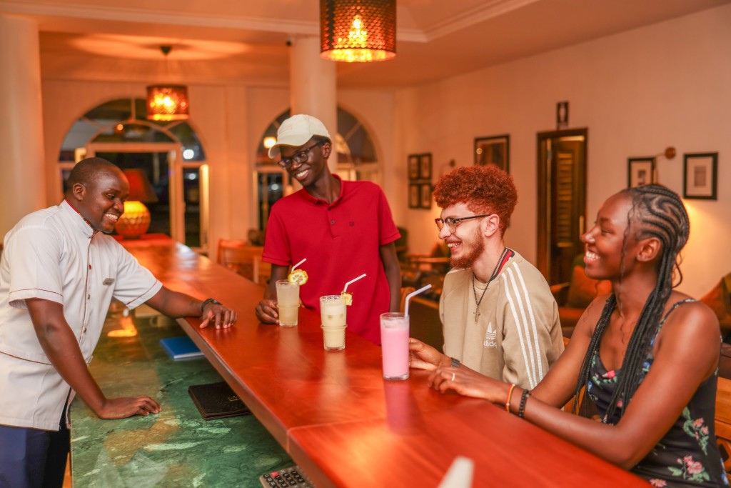 A member of bar staff serving three guests at the counter, drinks set out in front of them.