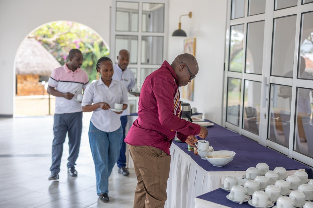 Delegates collecting tea at a refreshment table, flasks and rows of cups laid out along it.
