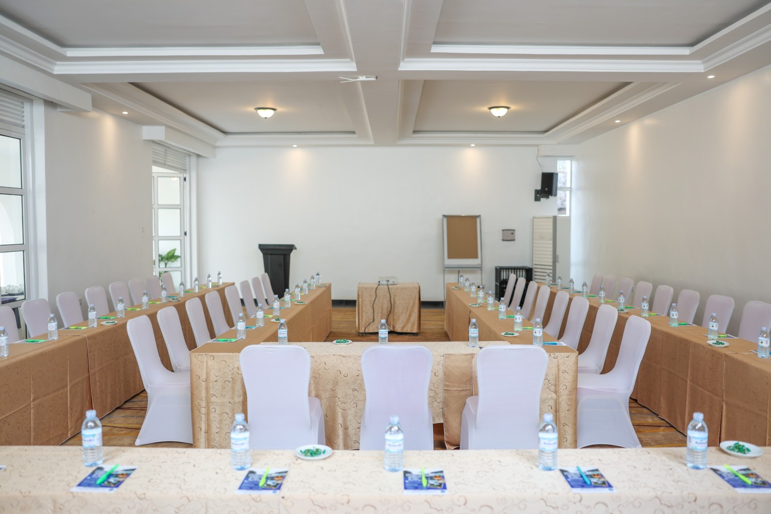 The conference hall dressed for a session, with covered chairs, notepads and water set out.