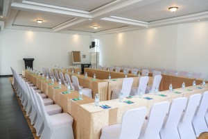 The conference hall dressed for a session, with covered chairs, notepads and water set out.