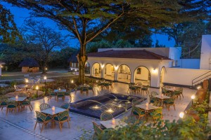 Candlelit tables and a lit water feature on the courtyard terrace at blue hour, the arcades glowing behind.