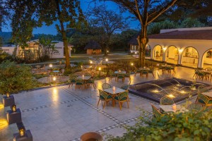 Candlelit tables and a lit water feature on the courtyard terrace at blue hour, the arcades glowing behind.