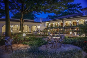 Candlelit tables and a lit water feature on the courtyard terrace at blue hour, the arcades glowing behind.
