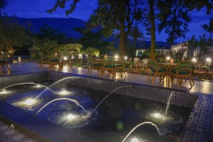 Candlelit tables and a lit water feature on the courtyard terrace at blue hour, the arcades glowing behind.