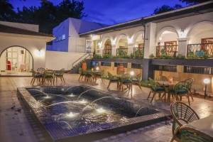 Candlelit tables and a lit water feature on the courtyard terrace at blue hour, the arcades glowing behind.
