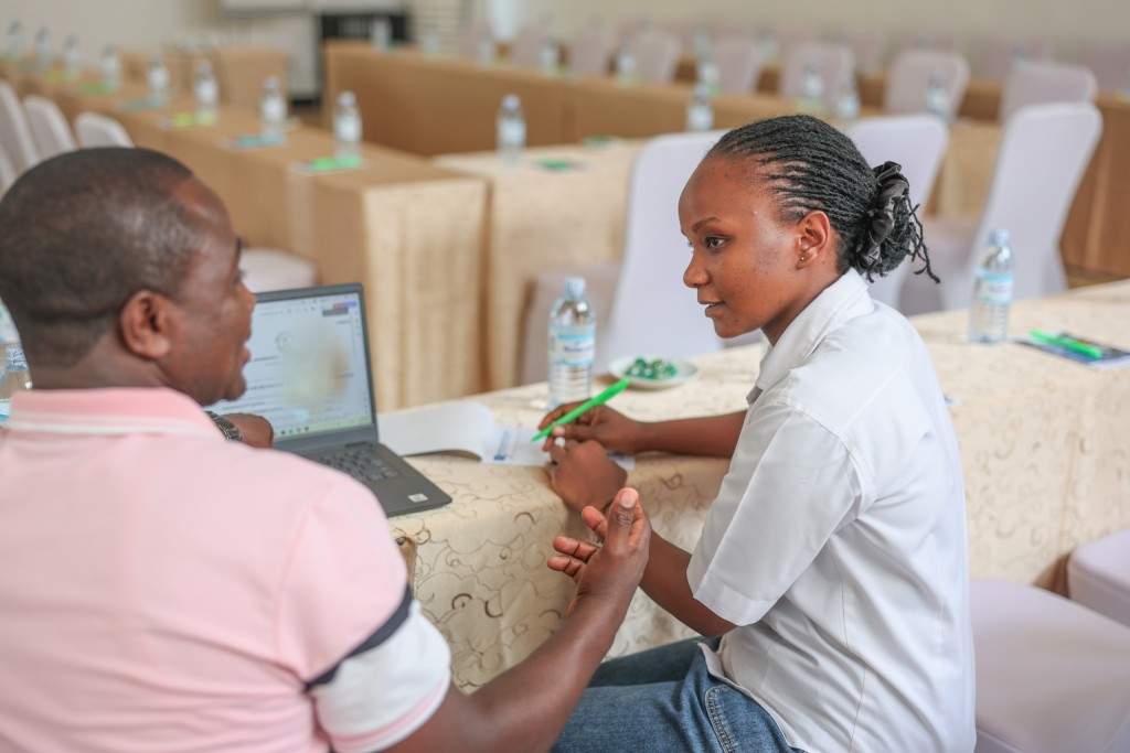 Two delegates conferring over an open laptop at a skirted conference table.