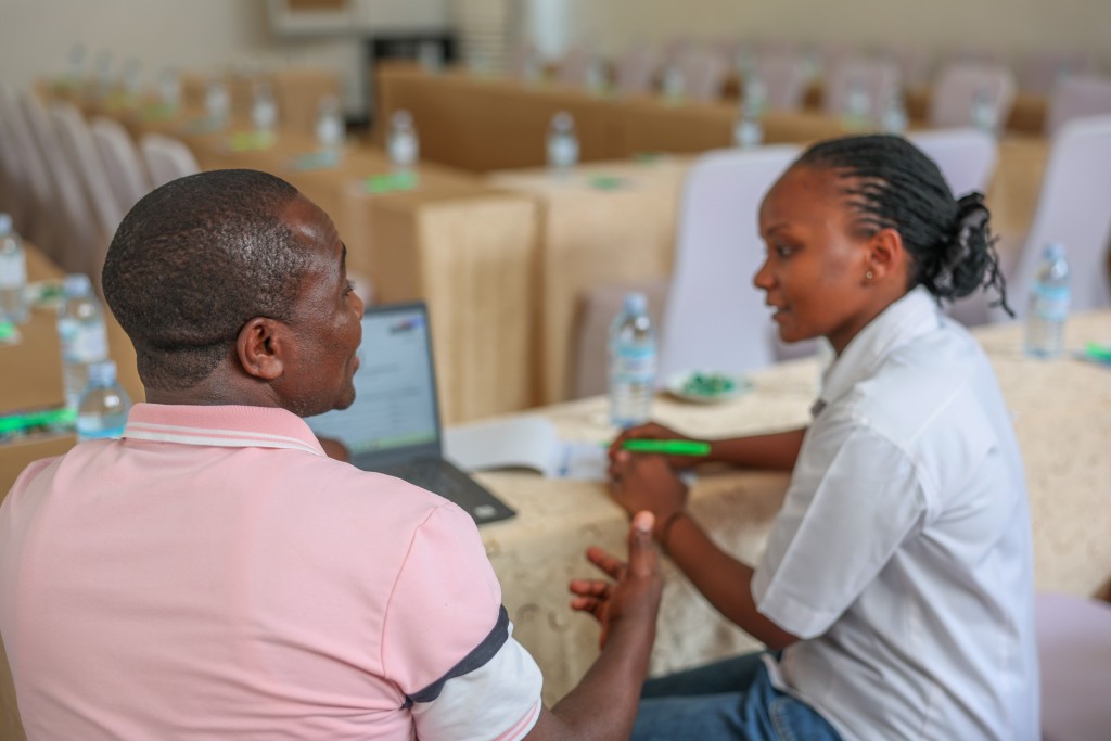 Two delegates conferring over an open laptop at a skirted conference table.