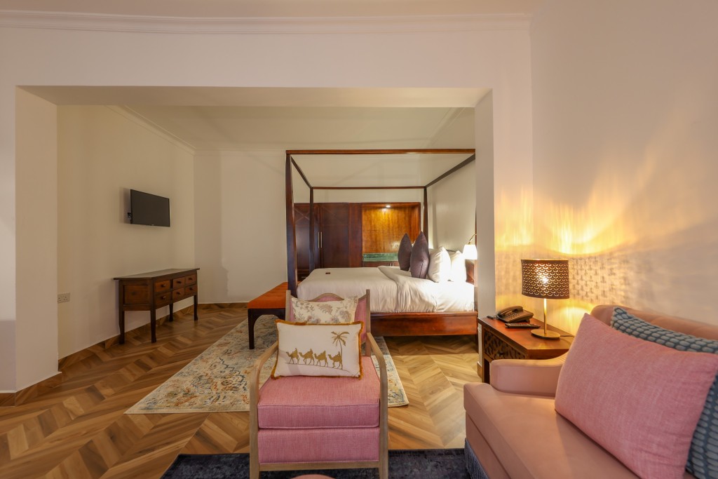 An Executive Suite with a four-poster bed, an armchair beside it and a sofa in the foreground.