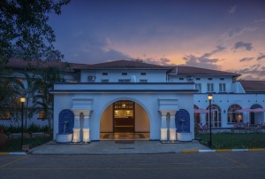 The symmetrical front elevation of the 1950s building at dusk, its central arch lit gold.