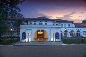 The symmetrical front elevation of the 1950s building at dusk, its central arch lit gold.
