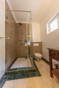 An en-suite bathroom with a glazed walk-in shower, twin basins and a marble-tiled floor.