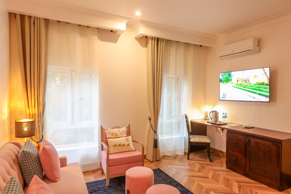 A guest room with a writing desk and wall-mounted television, an armchair and a kettle tray by the window.