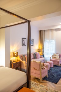 A guest room with sofa seating, writing desk, television and a window onto the garden.