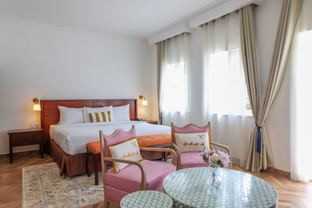 A guest room with a king bed, two armchairs and a small table set by the window in daylight.