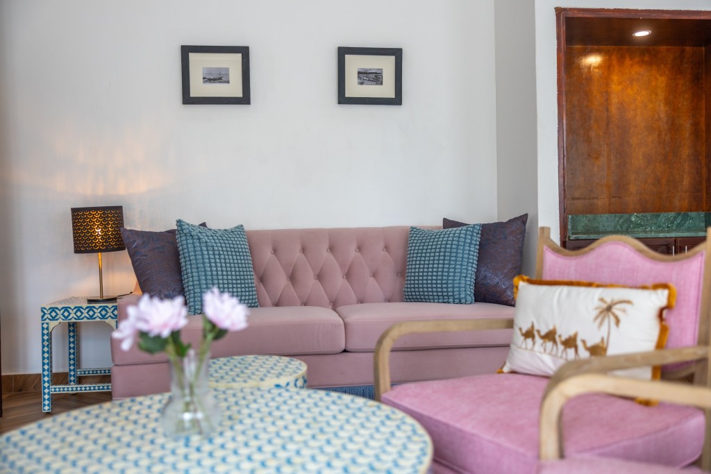 A guest room seating area with a pink sofa, flowers on a patterned round table and a tall timber wardrobe.