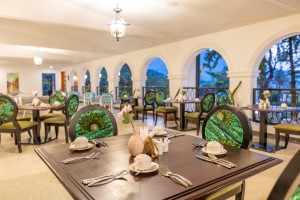 Masaaba Restaurant: tables and cane chairs along the arched veranda, hills and greenery through the openings.