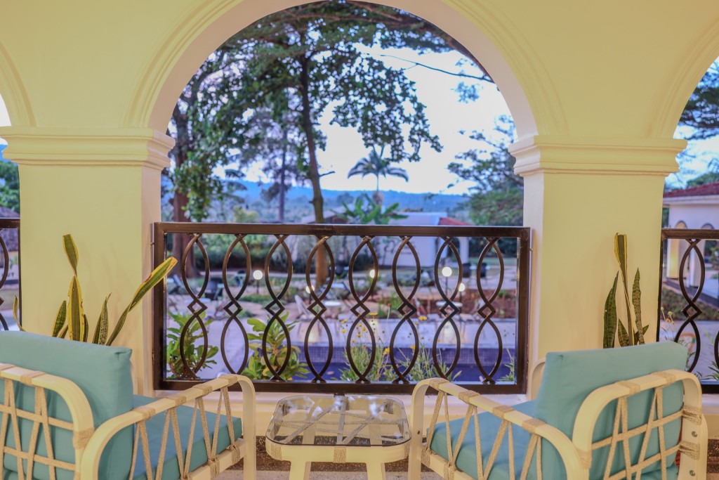 Cane armchairs and a low table on the restaurant balcony, framed by a tall arch open to the trees and the plain beyond.