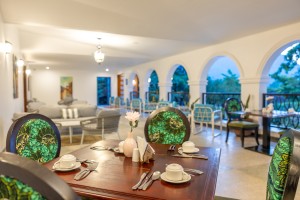 Masaaba Restaurant: tables and cane chairs along the arched veranda, hills and greenery through the openings.