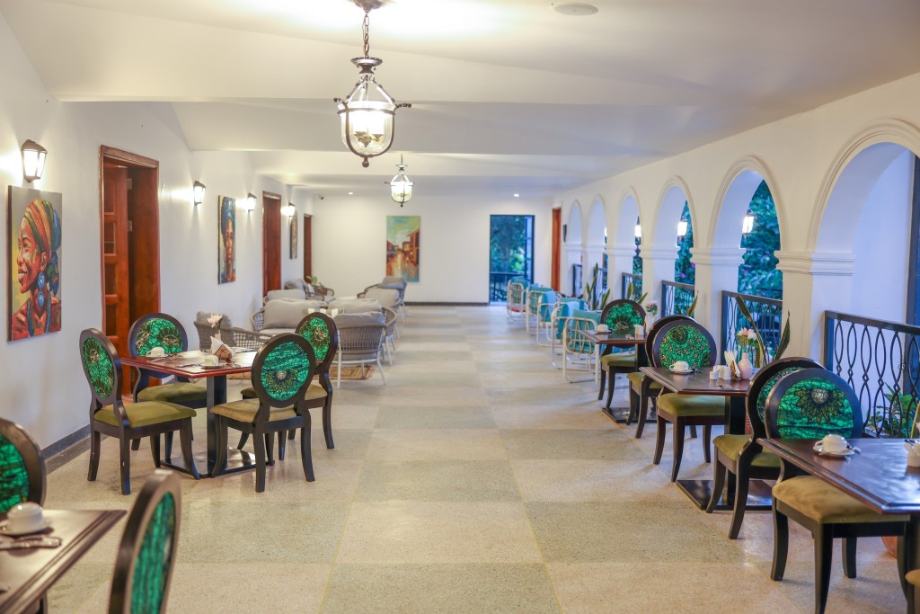 The dining room seen down its length, tables and cane chairs ranged along a run of arched windows.