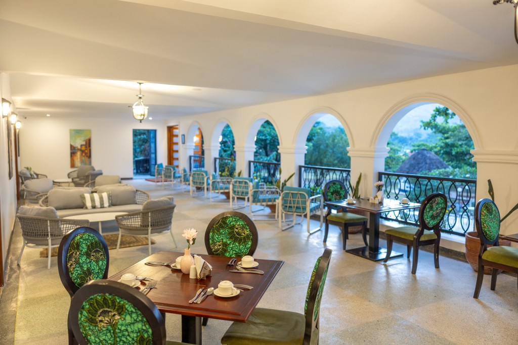 The long arcaded dining room, tables laid along the window side and lounge seating set back beyond them.