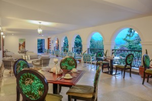 Masaaba Restaurant: tables and cane chairs along the arched veranda, hills and greenery through the openings.