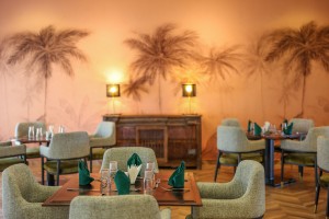 The dining room with its painted palm mural, teal napkins and carved timber furniture.