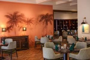 The dining room with its painted palm mural, teal napkins and carved timber furniture.