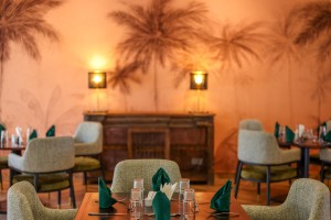 The dining room with its painted palm mural, teal napkins and carved timber furniture.