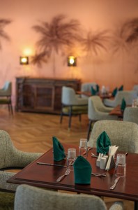 The dining room with its painted palm mural, teal napkins and carved timber furniture.