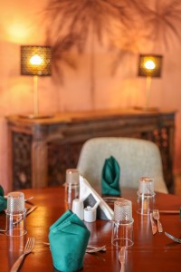 The dining room with its painted palm mural, teal napkins and carved timber furniture.