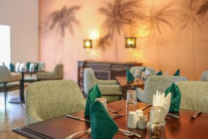 The dining room with its painted palm mural, teal napkins and carved timber furniture.
