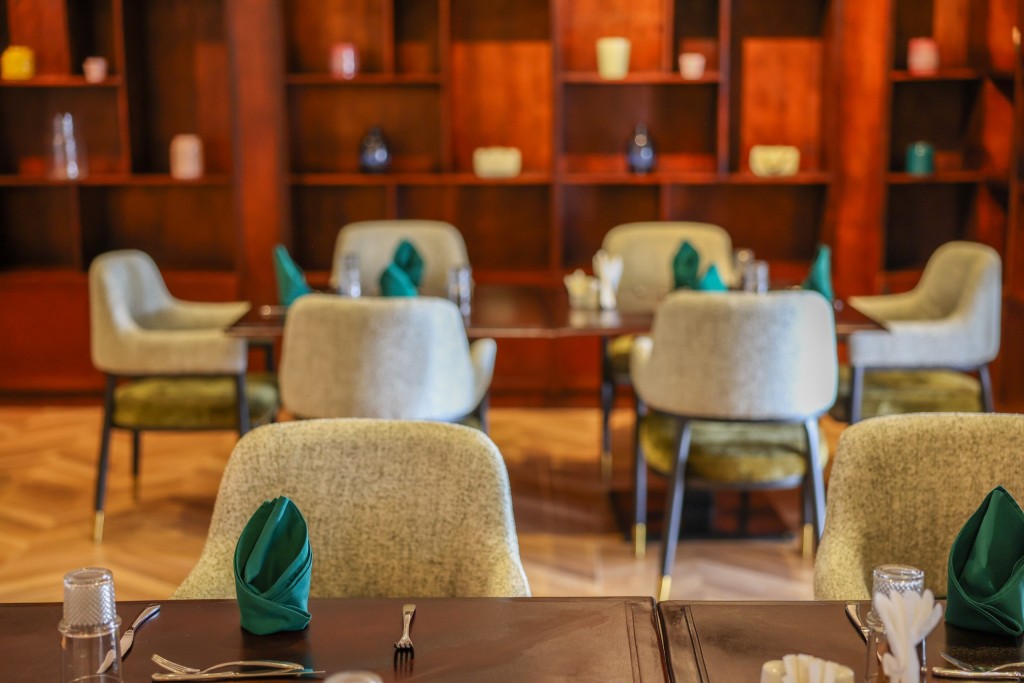 A timber-shelved room with upholstered armchairs drawn up to tables laid with green napkins.
