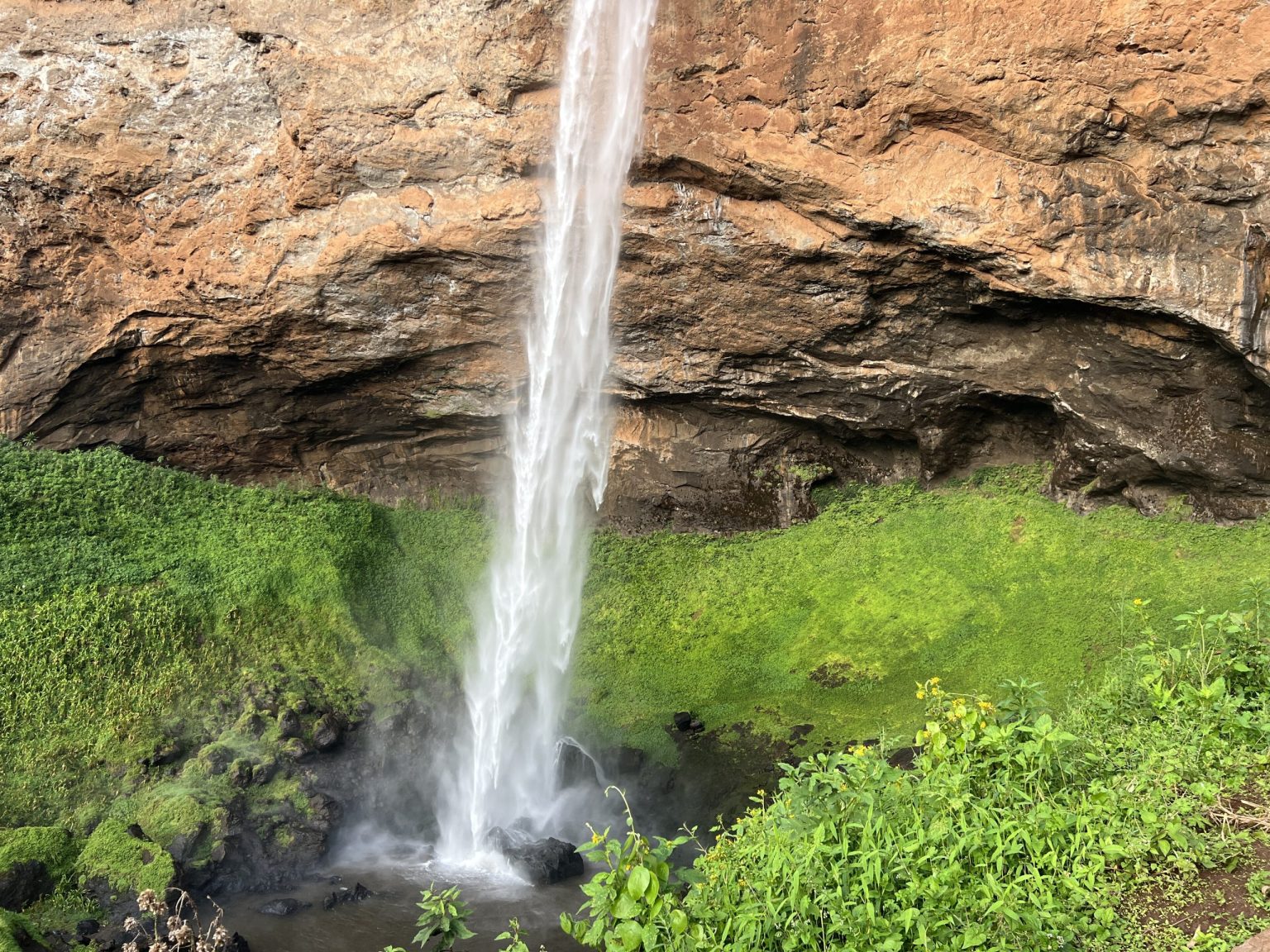 The base of a Sipi waterfall striking mossy green rock below an overhanging cliff.