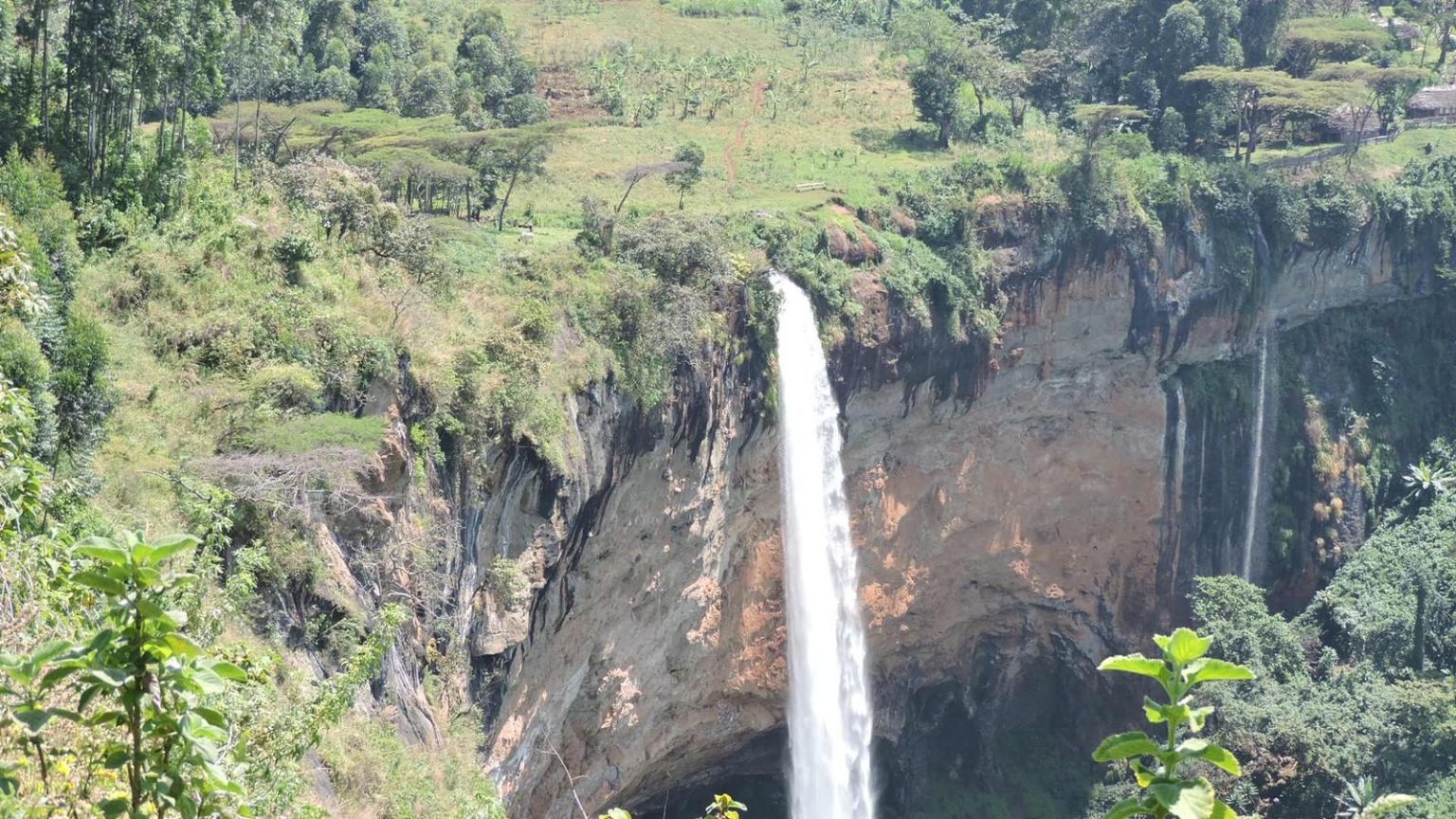 Sipi Falls pouring over the escarpment with farmland along the cliff top.