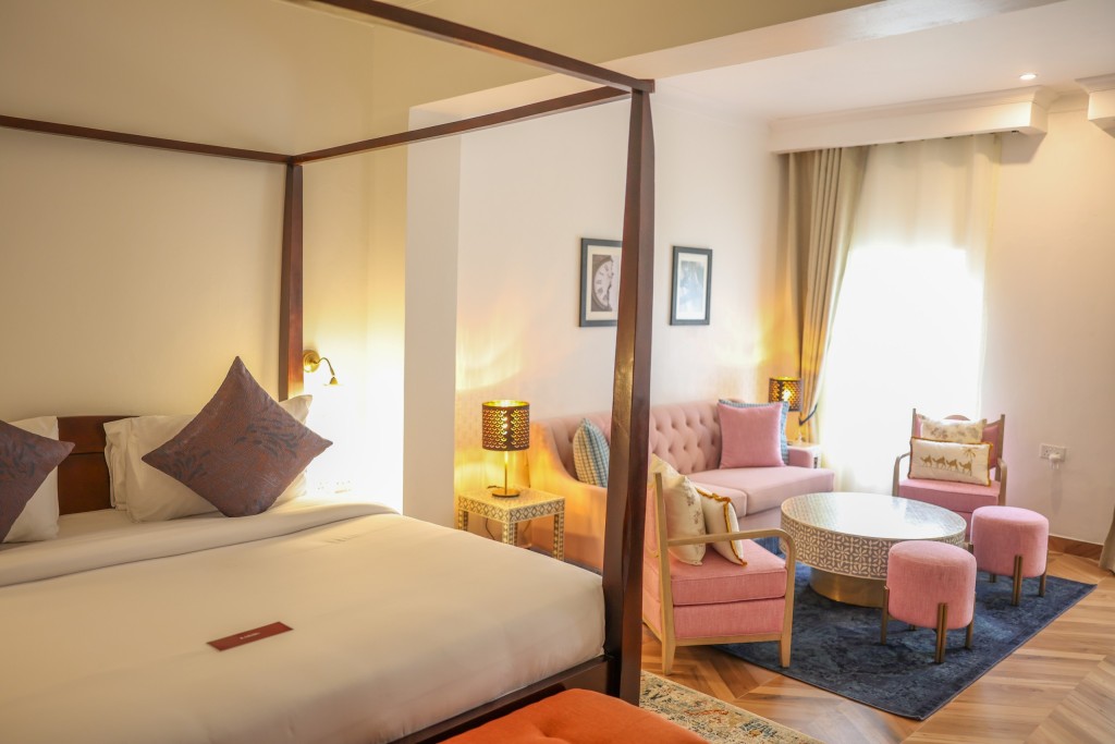 A suite with a four-poster bed at one end and a sofa, armchairs and round table at the other.
