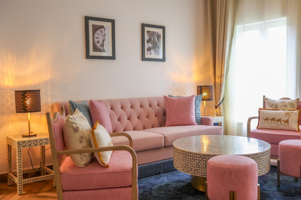 A suite lounge with a buttoned sofa, two armchairs and a patterned round table under a shaded lamp.