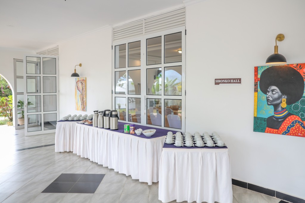 A long skirted table set with vacuum flasks and rows of cups and saucers along a wall of windows.