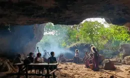 People seated together around a fire inside a large rock cave on the slopes of Mount Elgon.