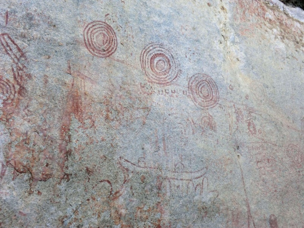 Red concentric circle paintings on the pale rock face at the Nyero site.